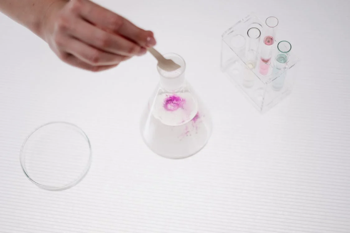 A person's hand adding a substance to a conical flask full of liquid.