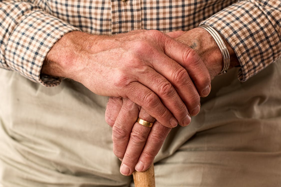 An elderly gentleman's hands holding a walking stick.