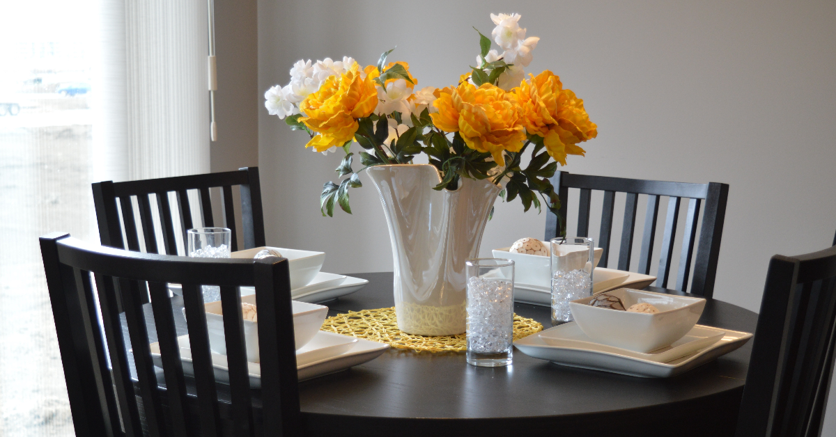 A round dining table, set and with a vase of flowers in the middle.