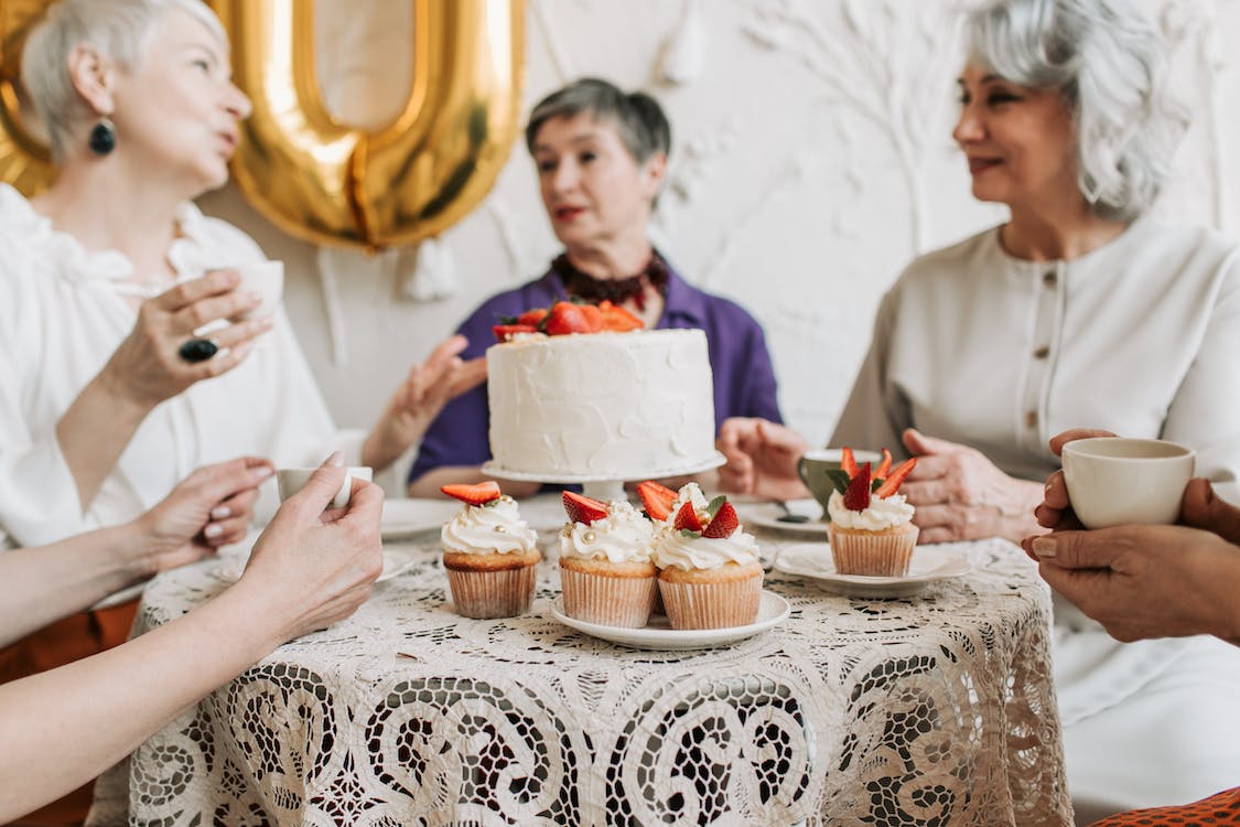 Four older ladies celebrating a birthday with cakes and tea.