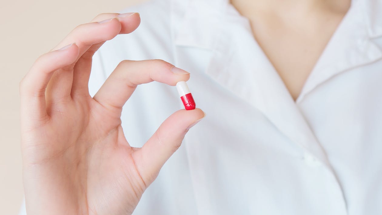 A hand holding a red and white capsule between its thumb and index finger.