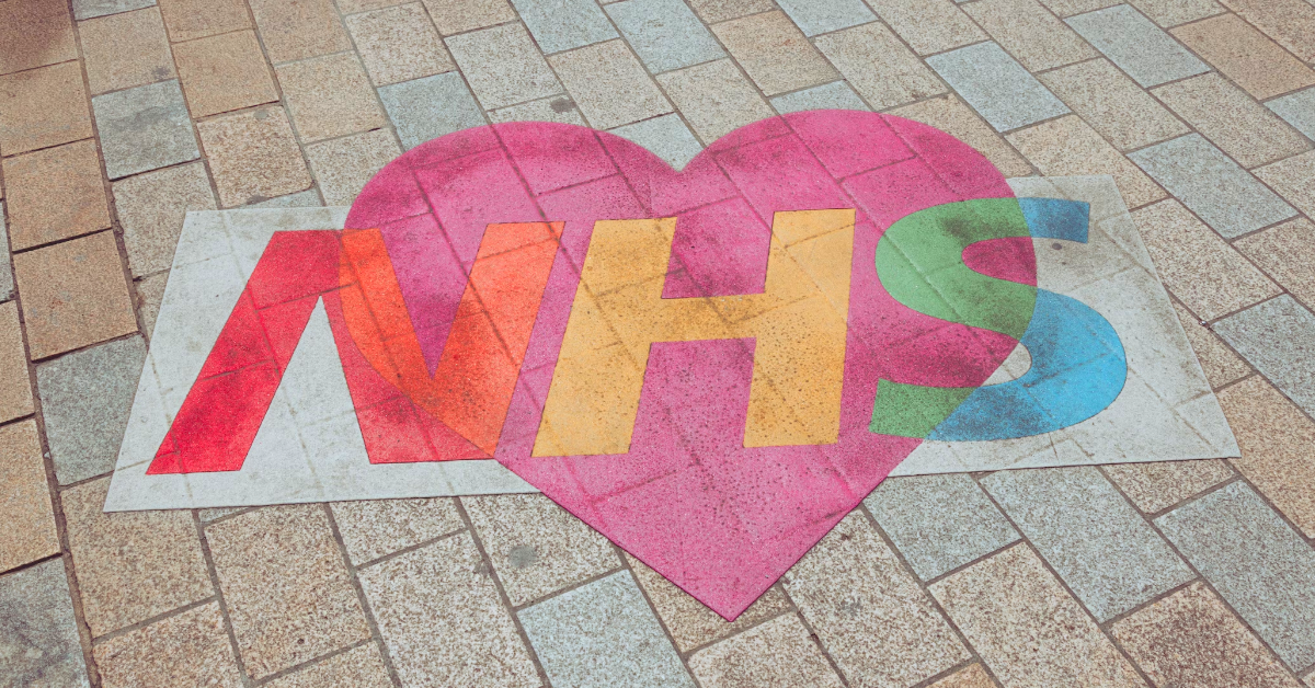 A multi-coloured NHS logo overlayed on a pink love heart.