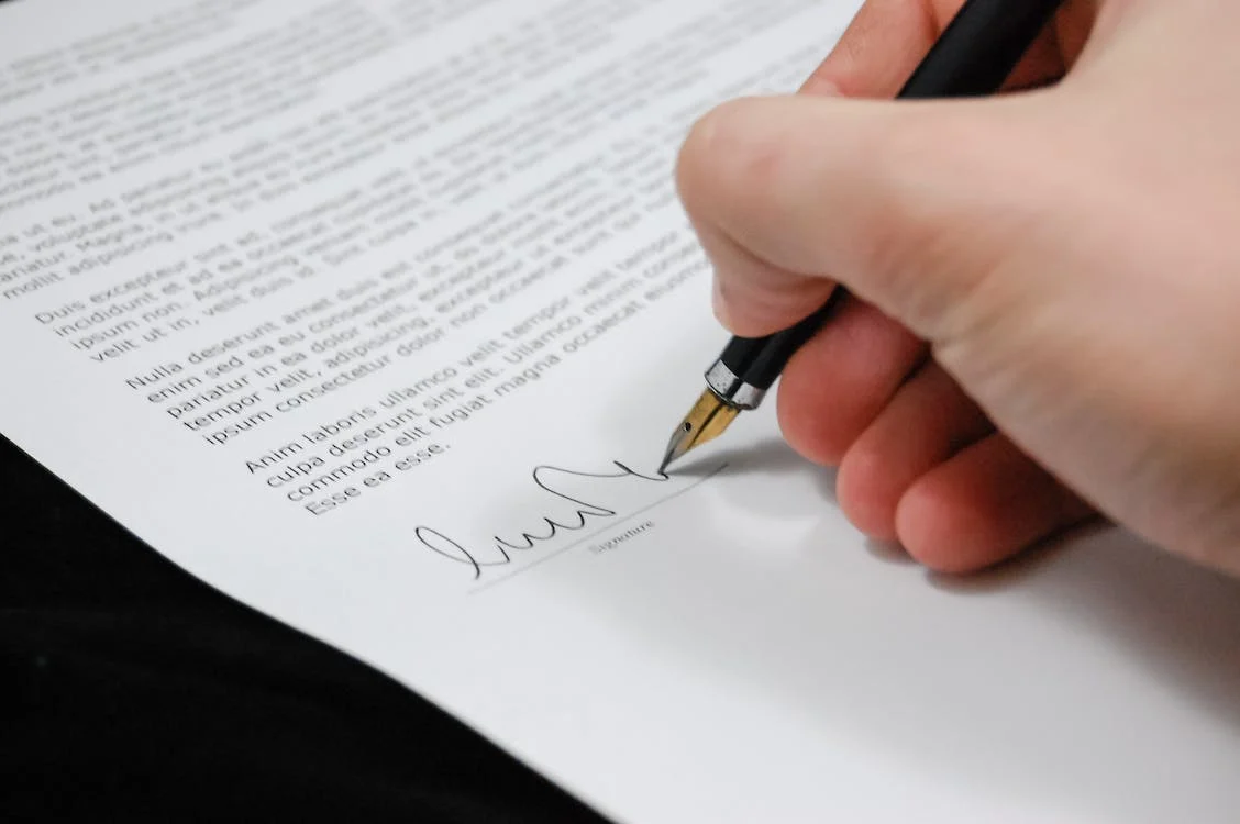 A hand holding a pen and signing a document.