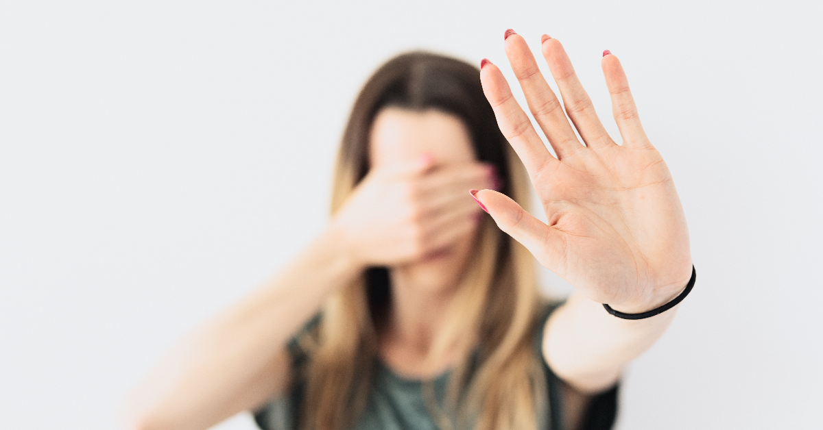 A person holding up their left hand and covering their eyes with the other.